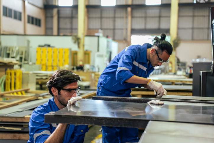 Two male workers are busy completing full service metal part assembly.